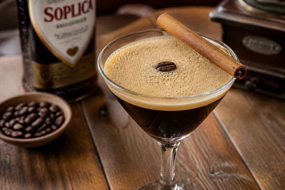 Espresso martini z pianką i ziarnem kawy, ozdobione laską cynamonu obok butelki Soplica