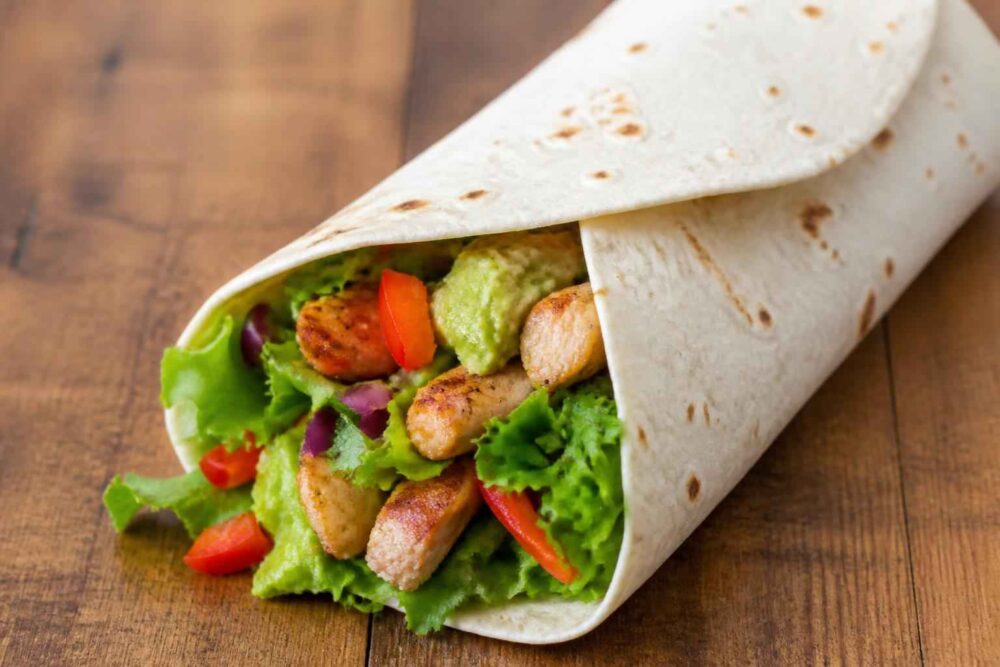Tortilla z grillowanym kurczakiem, sałatą, guacamole, papryką i pomidorem na drewnianym stole